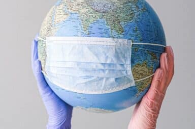 Globe with a medical mask on held up by two gloved hands