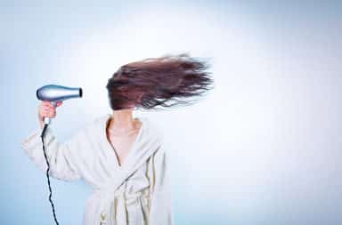 Woman pointing a hair dryer at her face
