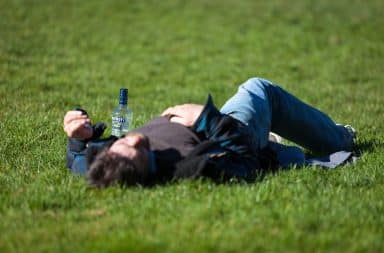 Man laying in the grass hungover with a bottle of Smirnoff vodka liquor
