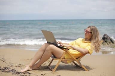 Woman typing at a laptop on the beach in a chair