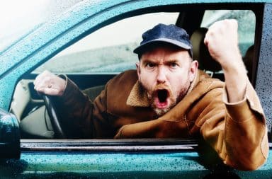 Man holding his fist out the open window of a car angrily