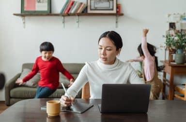 Mother working at a laptop at home while her two children are playing